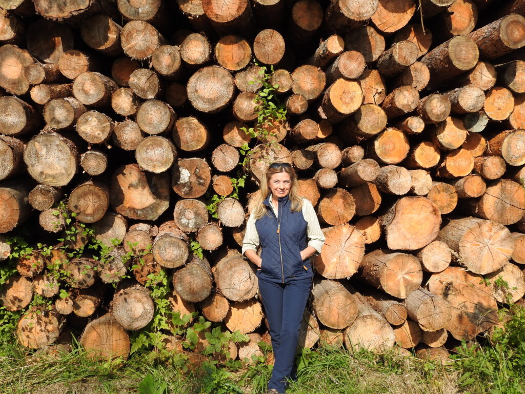 Christa Kummer lehnt an einem Holzstoß.