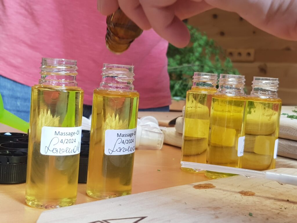 5 kleine Fläschchen mit Aufschrift "Massageöl Lavendel" auf einem Tisch. in eines wird noch Öl geträufelt