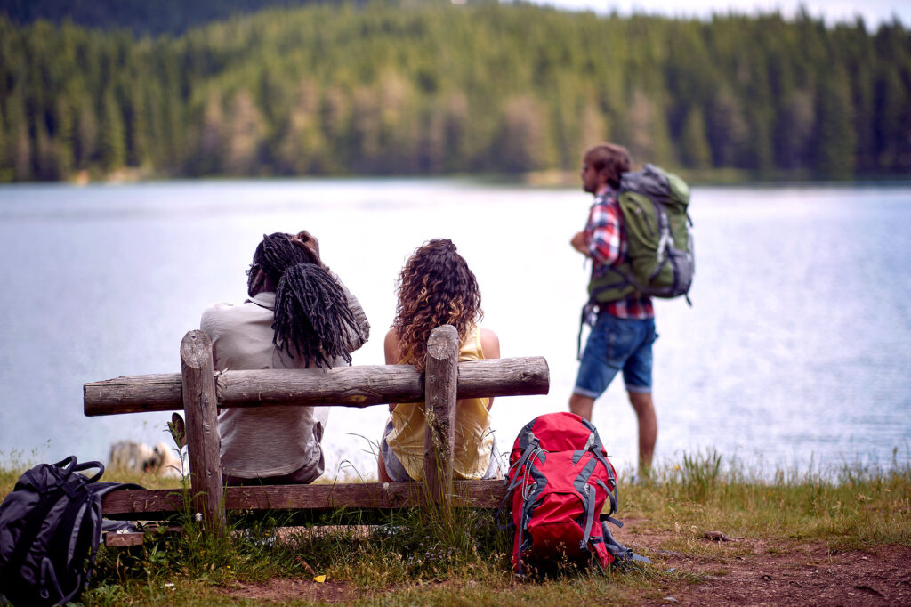 Drei Wanderer an einem See mit Wald im Hintergrund