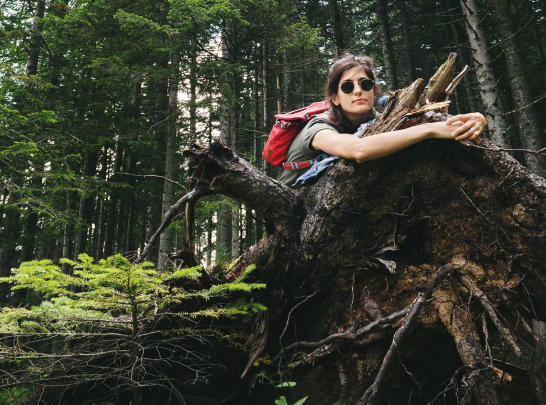 Frau mit Sonnenbrille, die im Wald einen Baumstumpf umarmt.