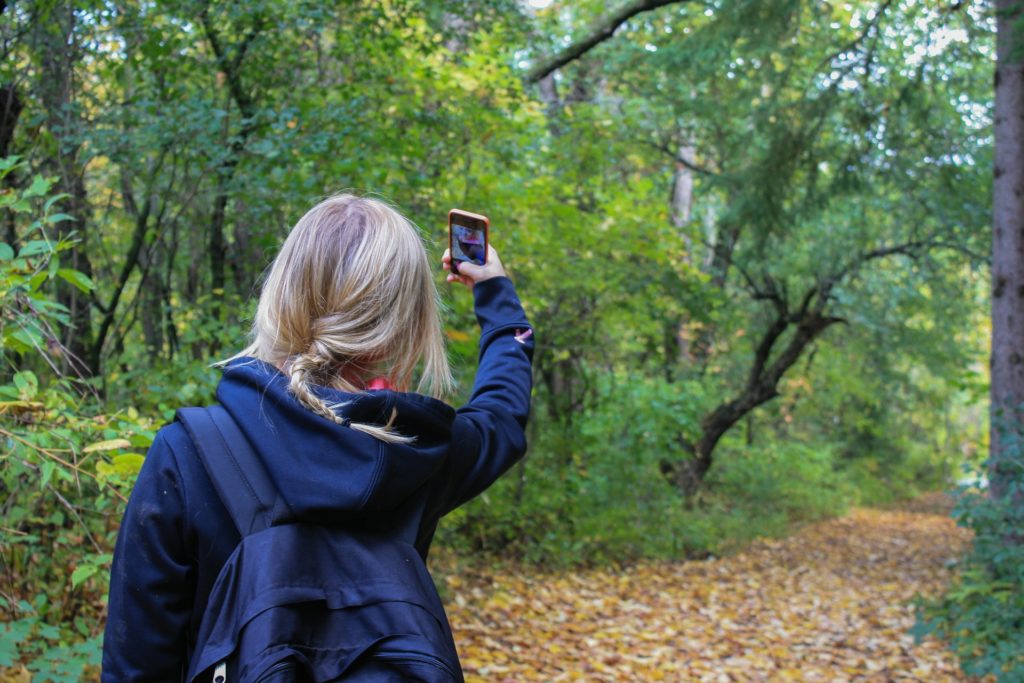 Mädchen steht im Wald und hält ein Handy in die Luft